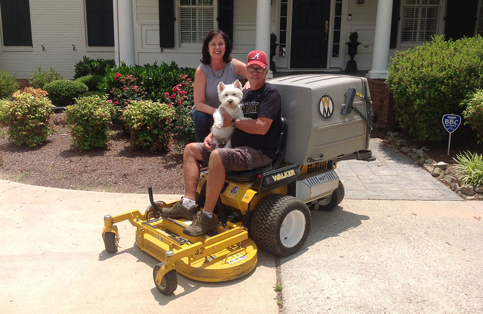 Harry Stokes, owner of Yard Perfect, sits on a Walker Mower with his wife, Barbara, and his dog.